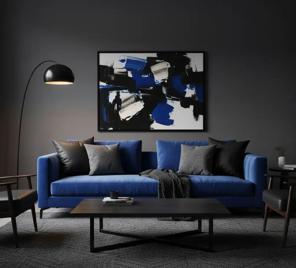 A royal blue sofa set against a backdrop of rich, dark charcoal grey walls. The furniture includes sleek black side tables and a coffee table, and the sofa is accented with black and white graphic pillows, creating a dramatic, luxurious, and modern aesthetic.